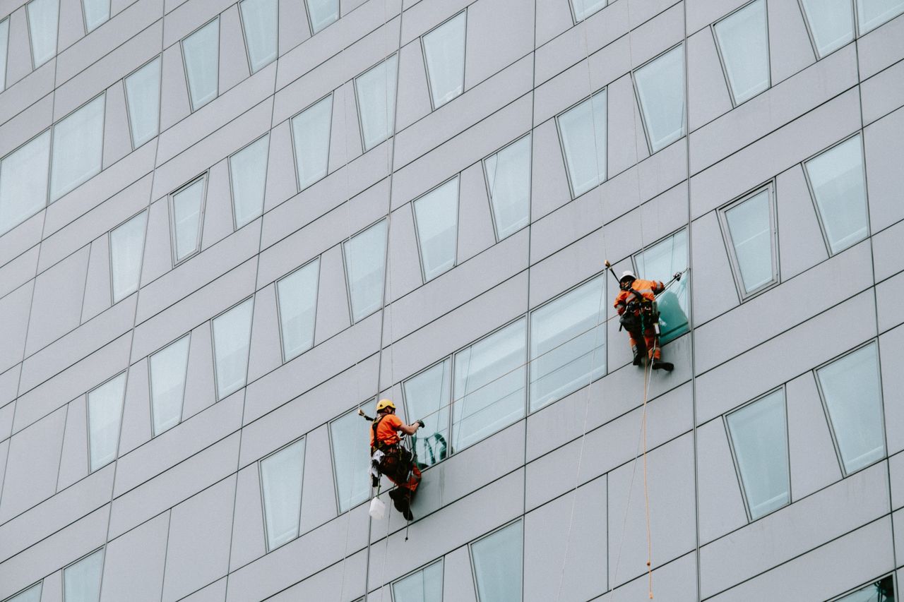 Des laveurs de vitres en hauteur, équipés de protections, nettoient la façade d’un gratte-ciel.